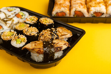Delicious sushi rolls in disposable boxes on a yellow background. Food delivery concept. Food in the office. Japanese food. Flat lay top view, with copy space and space for text.