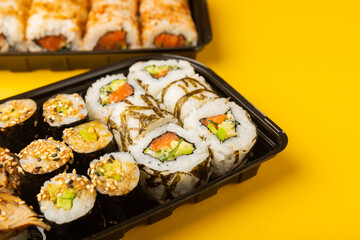 Delicious sushi rolls in disposable boxes on a yellow background. Food delivery concept. Food in the office. Japanese food. Flat lay top view, with copy space and space for text.