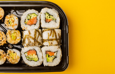 Delicious sushi rolls in disposable boxes on a yellow background. Food delivery concept. Food in the office. Japanese food. Flat lay top view, with copy space and space for text.