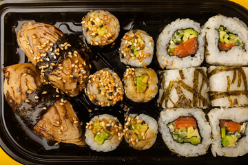 Delicious sushi rolls in disposable boxes on a yellow background. Food delivery concept. Food in...