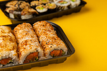 Fototapeta na wymiar Delicious sushi rolls in disposable boxes on a yellow background. Food delivery concept. Food in the office. Japanese food. Flat lay top view, with copy space and space for text.