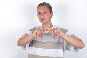 young woman with short hair wearing striped t-shirt over white background has rejection angry...
