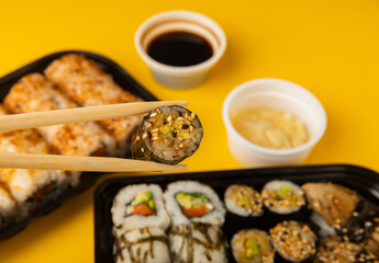Delicious sushi rolls in disposable boxes on a yellow background. Food delivery concept. Food in...