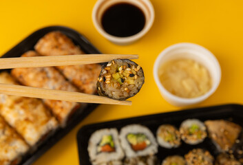 Delicious sushi rolls in disposable boxes on a yellow background. Food delivery concept. Food in the office. Japanese food. Flat lay top view, with copy space and space for text.