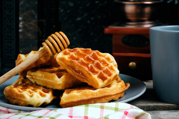 Waffles sweet pastries on plate, against background coffee grinder and decorative lamp with candle.