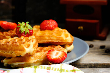 Waffles with strawberries and honey, sweet pastries on plate, against background coffee grinder.