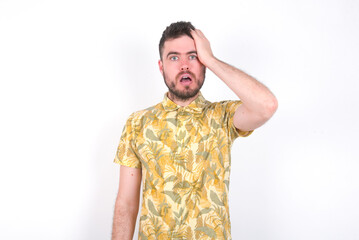 Portrait of confused young handsome bearded man wearing flowered shirt over white wall holding hand on hair and frowning, panicking, losing memory. Worried and anxious can not remember anything.