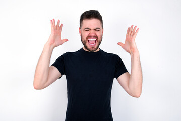 young caucasian bearded man wearing black t-shirt standing over white wall goes crazy as head goes...