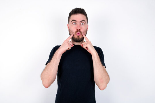young caucasian bearded man wearing black t-shirt standing over white wall crosses eyes and makes fish lips funny grimace