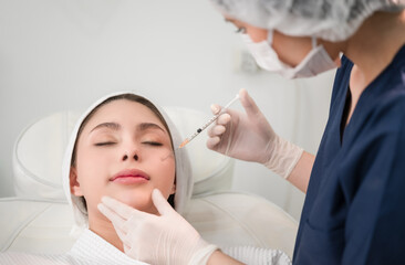 Beautiful young Asian woman getting cosmetology treatment facial skin injection by doctor beautician in beauty clinic.