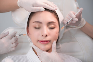 Young Asian woman getting cosmetology treatment facial skin injection by doctor beautician in...