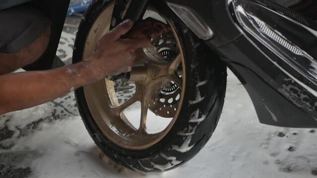 Worker doing detailed cleaning and washing a motorbike with foam soap in car wash station.