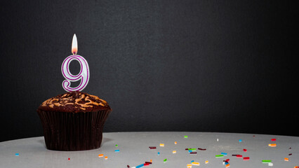 Muffin on black with a number from a candle number 9. Copy space, a pie on a black background, a...
