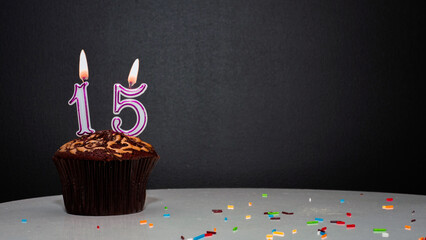 Muffin on black with a number from a candle number 15. Copy space, a pie on a black background, a...
