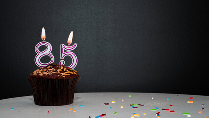 Muffin on black with a number from a candle number 85. Copy space, a pie on a black background, a...