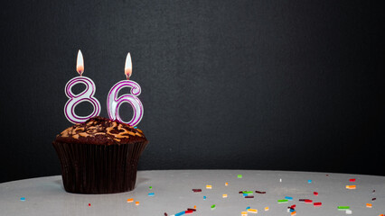 Muffin on black with a number from a candle number 86. Copy space, a pie on a black background, a...