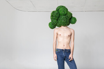 topless young guy in jeans stands in a mask in the form of a huge broccoli