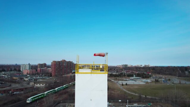 Aerial view of windsock with blue sky and city in the background. Slow rotation around conical tube flag for wind direction and speed. Used in airports and manufacturing facilities.