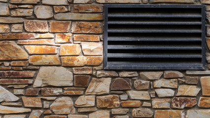 Nice colorful stone wall in beige, orange tones, and black air vent on the right, close up, background