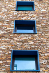 Orange stone wall and its three square windows, blue, seen from below