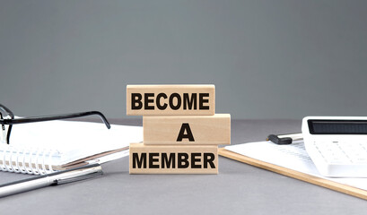 BECOME A MEMBER text on wooden block with notebook,chart and calculator, grey background
