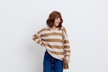 a close photo of a beautiful, stylish woman in a striped sweater and blue jeans posing relaxed standing on a light background with a bag worn over her shoulder