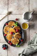 Pancakes with fresh berries, honey and linen napkin on pink tile background, flat lay