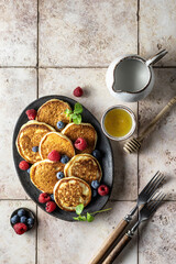 Pancakes with raspberry and blueberry, mint leave, honey and rustic cutlery on pink tile background, top view
