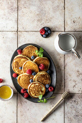 Pancakes with raspberry and blueberry, mint leave, honey and honey spoon on pink tile background, top view