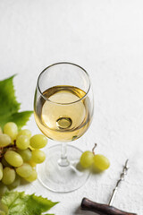 Glass of white wine with grapes and corkscrew on white background with text space