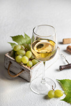 Glass of white wine with grapes, corks and corkscrew on white table background with text space