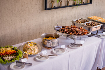 A table with a buffet of food served in stainless steel bowls with salads and meats