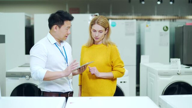 Asian male consultant Salesman Gives Professional advises female home appliance buyer in store. Shop assistant explaining washing machine to customer. showing modern electric in the supermarket