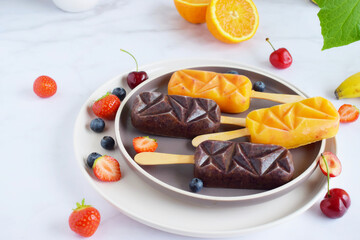 Self made popsicle with fruit pieces in it on a marble background