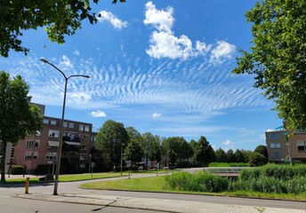 Rippled clouds named altocumulus undulatus over a neighbourhood in a Dutch town