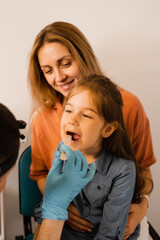 Oropharyngoscopy procedure for child. Otolaryngologist examines child throat with spatula. Family...