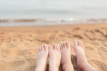 Close-up of woman and man's feet relaxing on sandy beach with lake in background