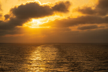 Fototapeta premium Setting sun illuminating the clouds over the wake of a cruise ship sailing down the coastline of Alaska