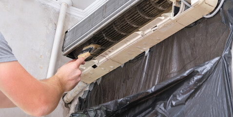 A man cleans an air conditioner with a brush. Split system maintenance.