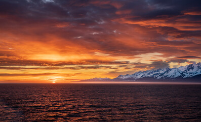 Fototapeta premium Sun on the horizon by the mountains and Mount Fairweather by Glacier Bay National Park in Alaska