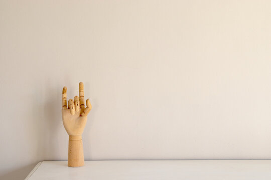 Wooden mannequin hand showing rock gesture against an empty beige wall with a lot of copy space.