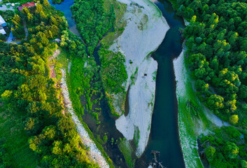 A rocky river in the middle of a forest. Aerial view of tranquil river reflecting sky, amid lush green landscape, aerial view. Top view of a mountain river in the forest.