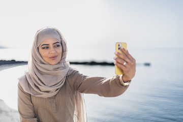 Muslim woman on the street using a phone and smiling