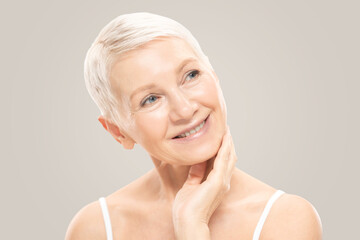 Beauty portrait of beautiful older woman with perfect fresh skin on her face, isolated on gray