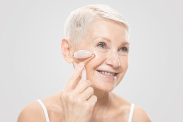 Beauty portrait of senior woman using facial roller massager for perfect skin on cheeks of her face