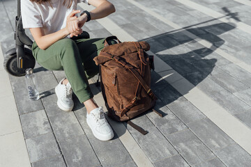 Woman in white sneakers and leather backpack sitting on electric scooter