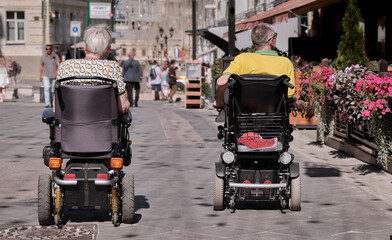 Accessible environment for people with disabilities. Happy family couple in motorized wheelchair are relaxing on city street using outdoor facilities for disabled.