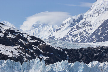 Glacier face with orbital cloud formation (lenticular clouds) in the mountain range behind