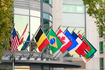 Row of world flags from global nationas hanging from short flag poles on a building 