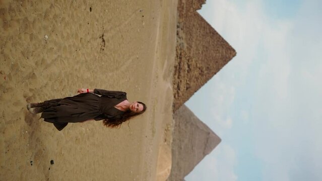 Vertical Instagram video. Young redhead girl in brown dress walking near piramids in Egypt, Cairo - Giza. Copy space